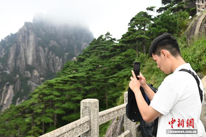 中国侨网8月12日,“徽风探源——2025华裔大学生中国文化体验营”走进安徽黄山风景区,学生们通过脚步丈量自然之美,沉浸式感受黄山生态与人文交织的独特魅力。图为华裔学生用手机记录黄山景色。中新社记者 韩苏原 摄